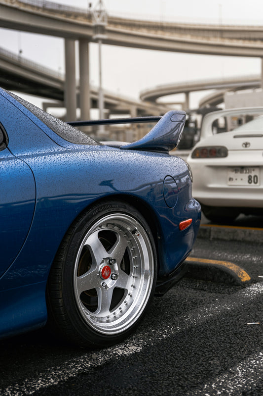 Blue sports car with chrome wheels in rain.